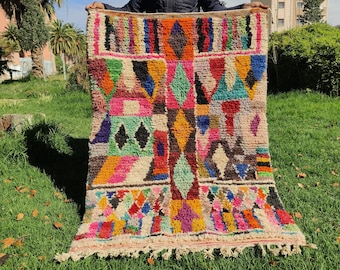 May include: A colorful Moroccan rug with geometric patterns in shades of pink, blue, green, yellow, and orange. The rug has a fringe border and is made of wool.