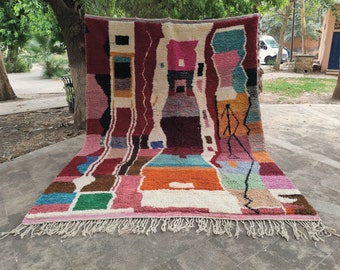 May include: A colorful abstract rug with a geometric design in shades of pink, red, orange, blue, green, and white. The rug has a fringe border.