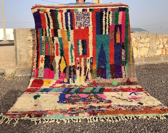 May include: A colorful Moroccan rug with a geometric pattern in shades of red, blue, green, yellow, and pink. The rug has a white background and is made of wool.