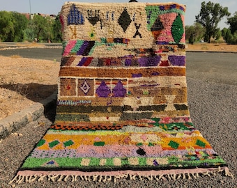 May include: A colorful Moroccan rug with geometric patterns and a fringe border. The rug is made of wool and has a variety of colors, including red, blue, green, yellow, and brown.