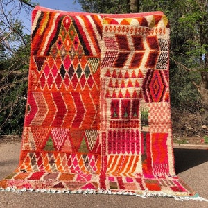 May include: A colorful Moroccan rug with a geometric pattern in shades of red, orange, pink, and white. The rug is woven with a variety of textures and is hand-knotted.