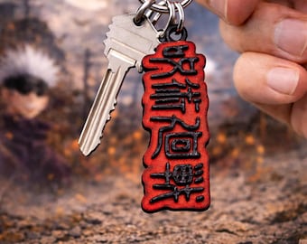 May include: A silver key and a red and black keychain with Japanese characters are held up. The keychain has a rectangular shape with a textured surface. The background is blurred, with a moon and a figure.