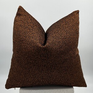 May include: A brown and black patterned throw pillow with a subtle shimmer. The pillow is square and has a zipper closure.