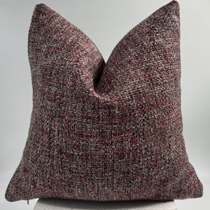 May include: A square pillow with a burgundy, black, and white tweed fabric cover.