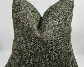 Könnte beinhalten: Ein quadratisches Zierkissen mit einem strukturierten Webstoff in Grün-, Braun- und Beigetönen. Das Kissen hat eine klassische Form und liegt auf einer weißen Oberfläche. Das Kissen ist etwa 45 cm groß.