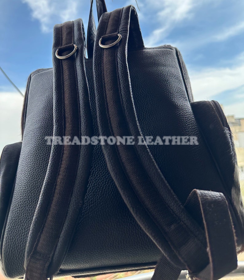 Pu&ograve; includere: Uno zaino in pelle nera con spallacci regolabili e una fibbia in metallo argentato. Lo zaino ha il testo "Treadstone Leather" stampato sul retro.