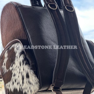 Pu&ograve; includere: Zaino in pelle marrone con una toppa in pelle di mucca sul davanti. Lo zaino ha due spalline regolabili e una tasca con cerniera sul davanti. Il testo "Headstone Leather" &egrave; visibile sul retro.