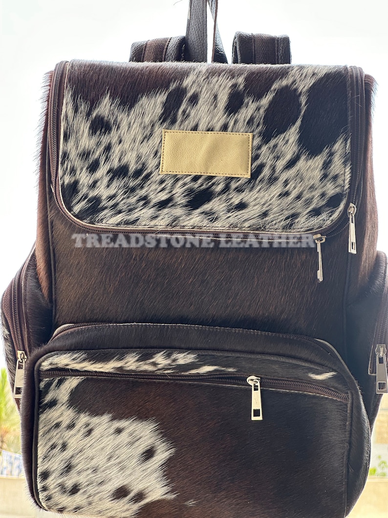 Pu&ograve; includere: Uno zaino in pelle marrone con un motivo in pelle di mucca bianca e marrone. Lo zaino ha un grande scomparto principale, una tasca anteriore pi&ugrave; piccola e due tasche laterali. Lo zaino ha anche una tracolla in pelle con una fibbia.