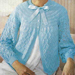 Könnte beinhalten: Ein hellblauer Strickcardigan mit einer weißen Schleife und Knopfleiste. Der Cardigan hat ein zartes Spitzenmuster und leicht bauschige Ärmel.