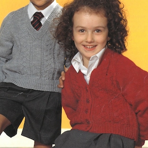 May include: Two children wearing knitted sweaters. The girl is wearing a red sweater with a button closure and the boy is wearing a grey sweater with a v-neck and a dark blue tie.