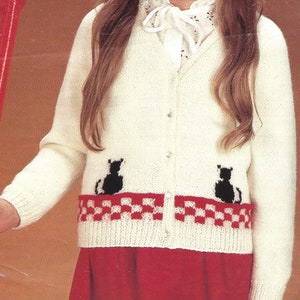 Op de afbeelding: Witte gebreide cardigan met zwarte katten silhouetten en een rood-wit geblokte band aan de onderkant.
