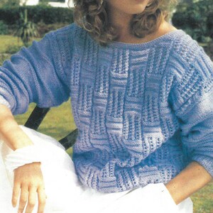 May include: A light blue knitted sweater with a geometric pattern. The sweater has a boat neck and long sleeves.