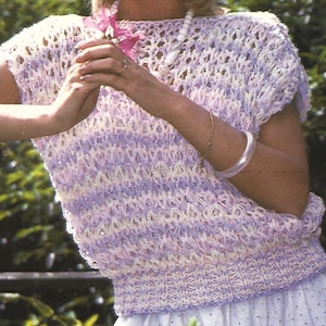 May include: A short-sleeved, open-weave top in shades of lavender, white, and pale yellow. The top has a ribbed waistband and a round neckline. The open weave design creates a textured look. The top is a light, airy garment.