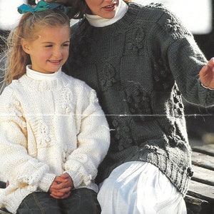 May include: Two people wearing white and grey knitted sweaters with a textured pattern. The sweaters have a round neckline and long sleeves.