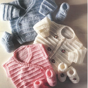 May include: Three knitted baby sweaters and six pairs of booties. The sweaters are in blue, white, and pink. The booties are in white and pink.