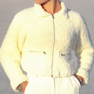 May include: A white, fluffy zip-up jacket with a stand-up collar and two zippered pockets.