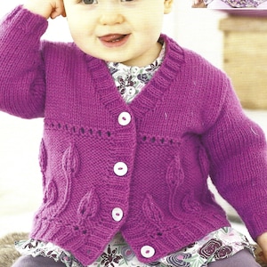 May include: A purple knitted cardigan with a button-up front and a leaf pattern. The cardigan is worn by a child.