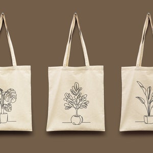 Pu&ograve; includere: Tre borse tote in tela bianca con disegni a linea nera di piante in vaso. Le piante sono una monstera, un ficus e un uccello del paradiso.