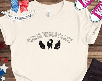 Pode incluir: Uma camiseta branca com o texto "Childless Cat Lady" em preto com três silhuetas de gatos pretos. O texto está em forma de arco.