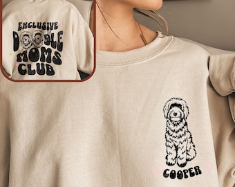 May include: A beige sweatshirt with a black doodle dog illustration and the name "Cooper" printed on the front. The back of the sweatshirt has the text "Exclusive Doodle Moms Club" printed in black.