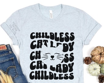 May include: Light blue t-shirt with a black graphic that says "Childless Cat Lady" in a retro font. The graphic also includes a stylized cat face with whiskers.