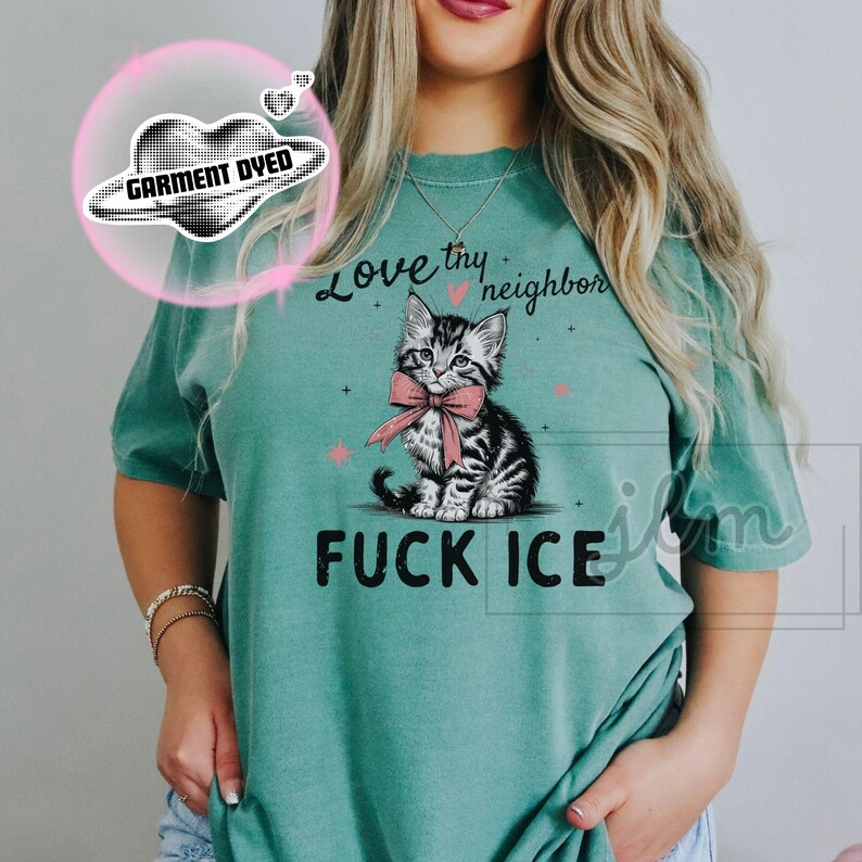 May include: Teal-colored t-shirt with a graphic of a kitten wearing a pink bow, and the text "Love thy neighbor" and "FUCK ICE". The shirt has a relaxed fit.