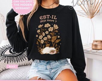 May include: Black sweatshirt with the text "EST-IL déjà mort?" and a floral and cat graphic. The sweatshirt also has the text "CAN YOU SPOT THE HIDDEN MESSAGE?" and "BLACK".