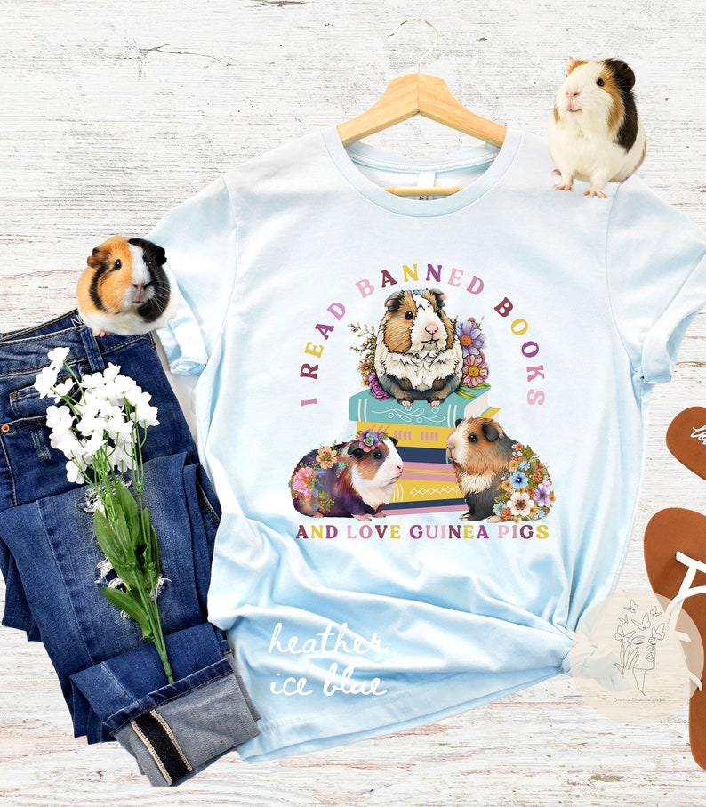 May include: Light blue t-shirt with the text "I read banned books and love guinea pigs" in a circle around a stack of books with three guinea pigs sitting on top. The guinea pigs are wearing flowers and the books are decorated with flowers.