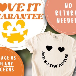 May include: Cream-colored t-shirt with a smiley face design. The eyes are black hearts, and the mouth is formed by the words "100% SATISFACTION". The shirt is part of a collection with a Halloween theme, as indicated by the pumpkin graphic.