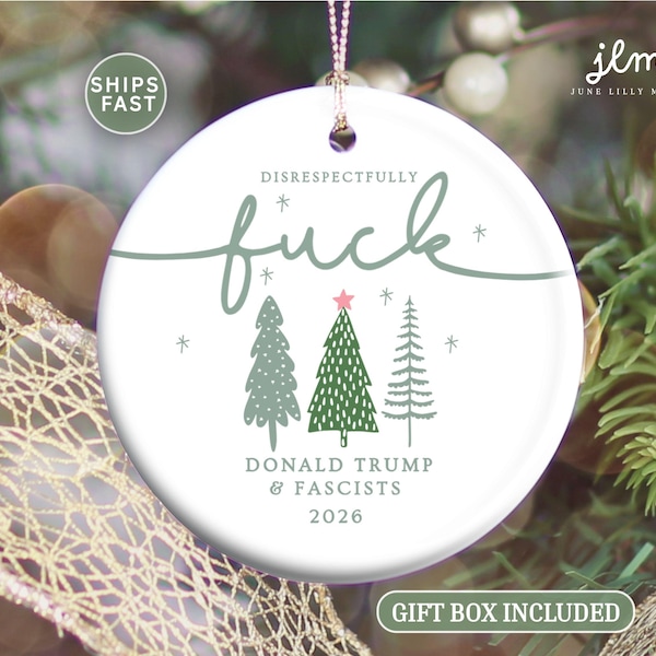 May include: A round white ceramic Christmas ornament featuring the text DISRESPECTFULLY fuck in green script, three stylised green pine trees, and the text DONALD TRUMP & FASCISTS 2026 in grey. The ornament hangs from a thin gold string.