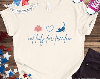 May include: A white t-shirt with a blue cat, a pink book, and a blue heart. The text "cat lady for freedom" is printed on the shirt.