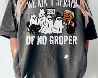May include: Dark gray t-shirt with a Halloween-themed graphic. The design features cartoon ghosts, a black cat, and a pumpkin-headed figure, with the text "WE AIN'T AFRAID OF NO GROPER" and "NOPE".