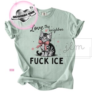 May include: Light green t-shirt with a graphic of a kitten wearing a pink bow, and the text "Love thy neighbor" and "FUCK ICE". The shirt also has a "Sustainably Made" logo.