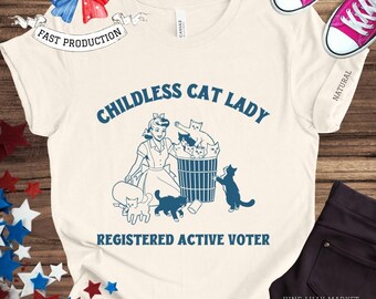 May include: A white t-shirt with the text "Childless Cat Lady Registered Active Voter" in blue lettering. The design features a cartoon woman with a group of cats in a trash can.