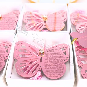 K&ouml;nnte beinhalten: Rosa schmetterlingsf&ouml;rmige Acryl-Ornamente mit einem dekorativen Strassstein in der Mitte. Die Ornamente haben ein ausgeschnittenes Design und zeigen arabische Kalligraphie und den Text "Welcome Baby Sumeyye".