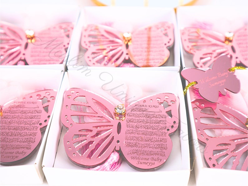 K&ouml;nnte beinhalten: Rosa schmetterlingsf&ouml;rmige Acryl-Ornamente mit einem dekorativen Strassstein in der Mitte. Die Ornamente haben ein ausgeschnittenes Design und zeigen arabische Kalligraphie und den Text "Welcome Baby Sumeyye".