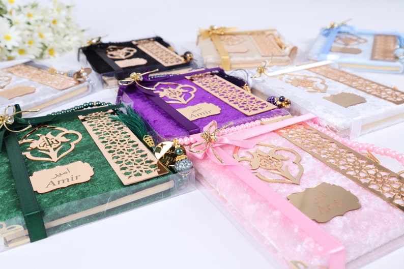 Op de afbeelding: Assortiment van gepersonaliseerde gebedenboeken, verpakt in fluweel met gouden accenten. Elk boek heeft een decoratief bladwijzer, een kwast en een naaminscriptie. De boeken zijn verkrijgbaar in groen, paars, roze, wit en zwart.