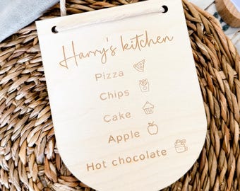 May include: A light-colored wooden sign with the text "Harry's kitchen" and food icons. The sign lists pizza, chips, cake, apple, and hot chocolate. A natural rope is attached for hanging.