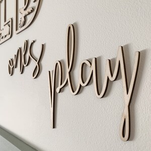 May include: Wooden wall decor with the words "Let ones play" in a cursive font.