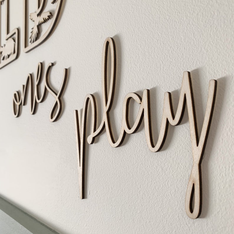 May include: Wooden wall decor with the words "Let ones play" in a cursive font.