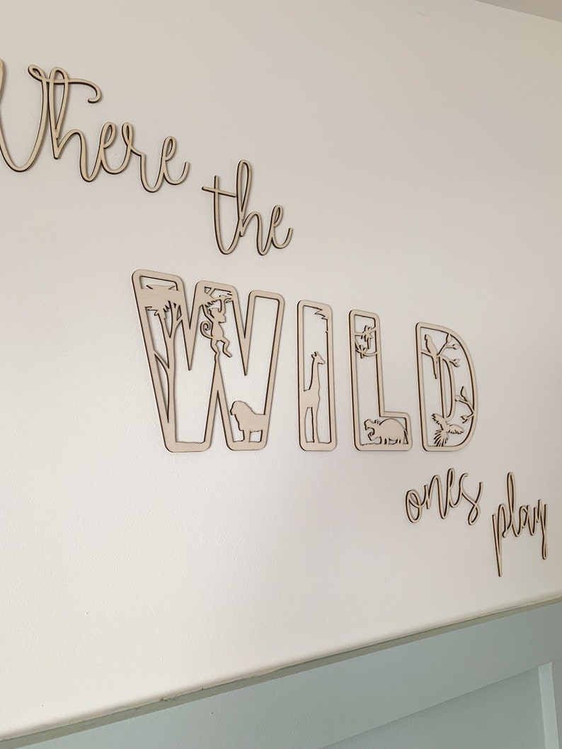 May include: Wooden wall decor with the words "Where the Wild Ones Play" in cursive script. The word "Wild" is made up of individual letters with cut-out animal silhouettes.