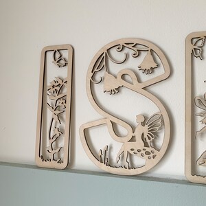 May include: Wooden letters spelling "ISI" with a fairy and floral design. Each letter is intricately cut with a fairy, flowers, and vines.