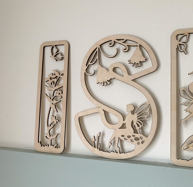 May include: Wooden letters spelling "ISI" with a fairy and floral design. Each letter is intricately cut with a fairy, flowers, and vines.