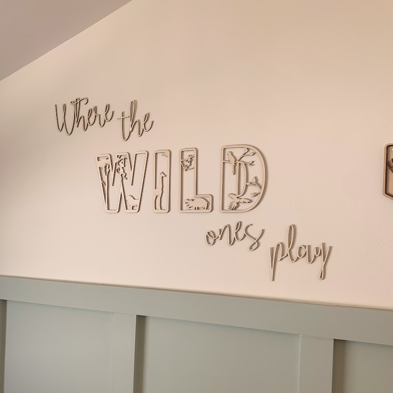 May include: Wooden wall decor with the words "Where the Wild Ones Play" in a cursive font. The word "Wild" is made up of individual letters with cut-out animal shapes.
