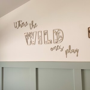 May include: Wooden wall decor with the words "Where the Wild Ones Play" in a cursive font. The word "Wild" is made up of individual letters with cut-out animal shapes.