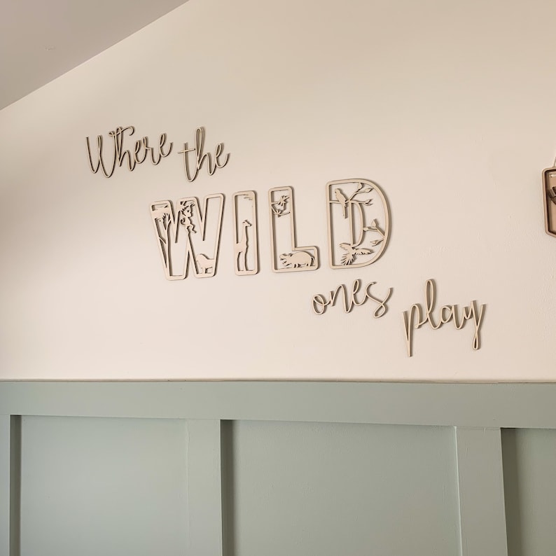 May include: Wooden wall decor with the words "Where the Wild Ones Play" in a cursive font. The word "Wild" is made up of individual letters with cut-out animal shapes.