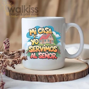 Puede incluir: Taza de cerámica blanca con asa, con el texto "Mi Casa y Yo Servimos al Señor" en letras coloridas. El diseño incluye una ilustración de una casa con tejado rojo, sobre un cielo azul y un paisaje verde.