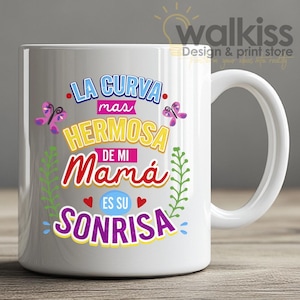 Puede incluir: Taza de cerámica blanca con asa curva. La taza presenta texto colorido en español: "LA CURVA mas HERMOSA DE MI Mamá ES SU SONRISA" con acentos de mariposas y hojas. La taza es un diseño de "walkiss Design & print store".
