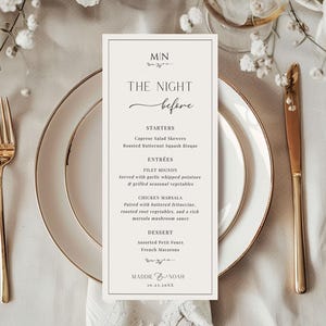 May include: A wedding menu card with a minimalist design. The card is placed on a white plate with gold trim, alongside gold cutlery. The menu lists starters, entrées, and dessert options, with the names of the couple and the date at the bottom.