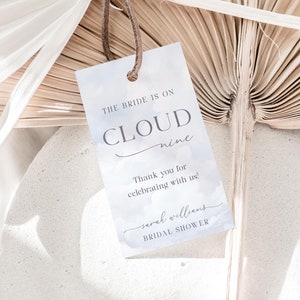 May include: A light blue bridal shower favor tag with the text "THE BRIDE IS ON CLOUD nine" and "Thank you for celebrating with us!"  The tag also includes the name "sarah williams" and the text "BRIDAL SHOWER".